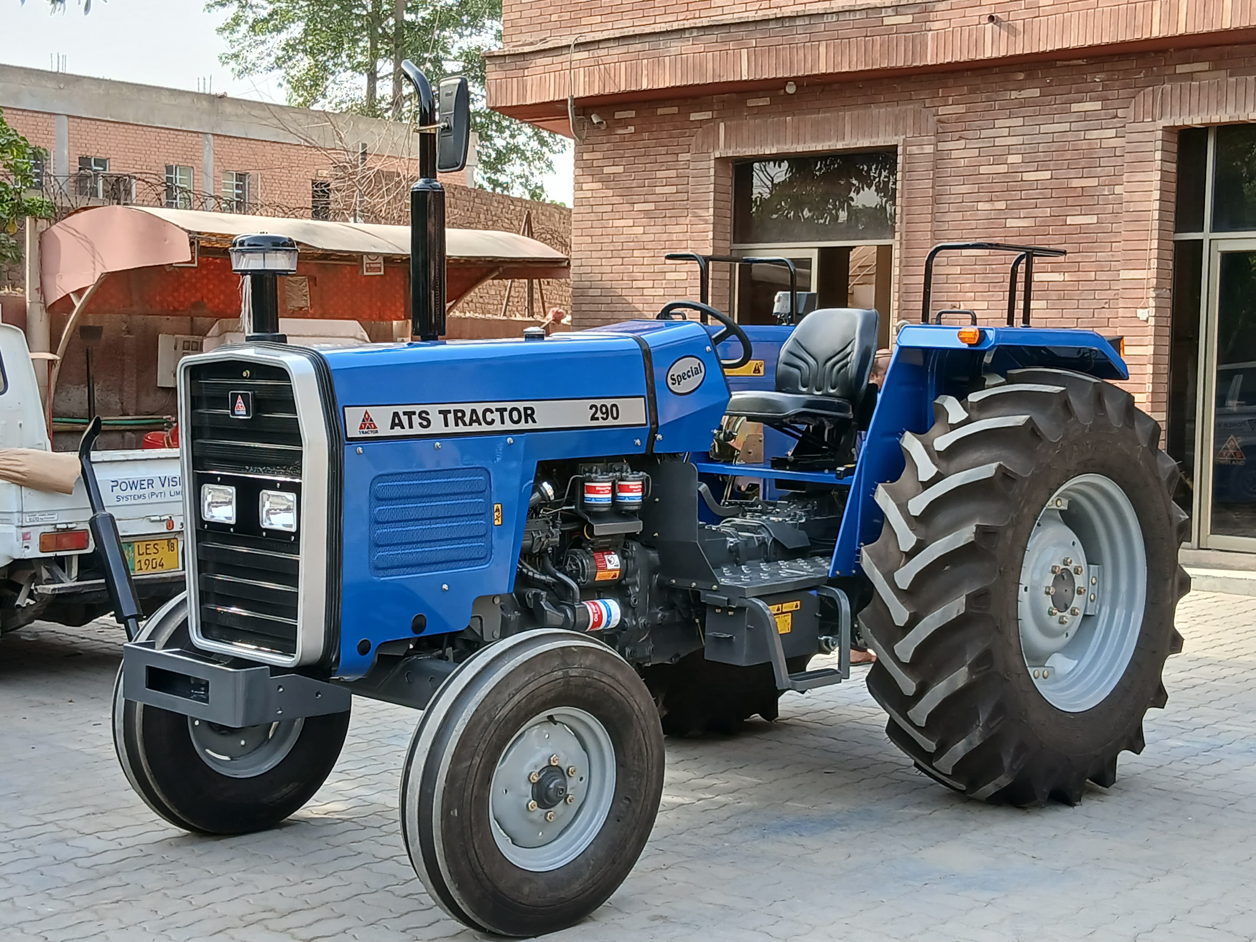 ATS Tractor 290 - Blue 77 HP 2WD tractor displayed in industrial courtyard with brick buildings, showing the Special model variant